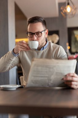 Restoran masasında oturmuş gazete okuyup kahve içen düşünceli bir adamın portresi.