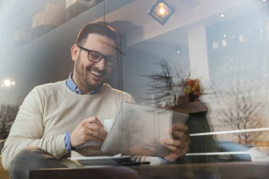 Yakışıklı genç adam restoran masasında oturuyor, kahve içiyor ve tablet bilgisayar kullanıyor.