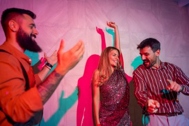 Bir grup neşeli genç bir partide dans edip şarkı söylüyor.