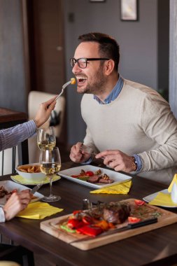 Bir çift restoranda yemek yiyor, birbirlerinin yemeklerini tadıyor ve eğleniyorlar.