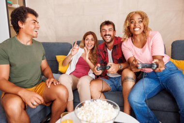 Bir grup neşeli genç arkadaş evde boş zamanlarını geçirirken video oyunları oynayarak eğleniyorlar.