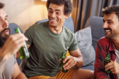 Bir grup erkek evde vakit geçirip, televizyon izleyip, bira içerek eğleniyor.