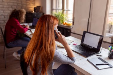Modern bir ofiste çalışan iş adamları, dizüstü bilgisayarda çalışan bir erkek ile telefon görüşmesi yapan kadınlar, birlikte çalışan serbest çalışanlar.