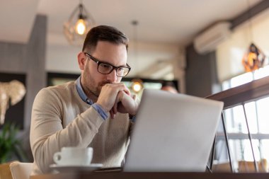 Restoran masasında oturan, kahve içen ve dizüstü bilgisayar üzerinde çalışan serbest çalışan bir erkek portresi.