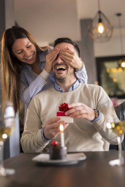 Lokantada buluşan çift, erkeğin doğum gününü kutlayan kadın, erkeğin gözlerini tutan ve ona bir hediye veren kadın ve küçük sürpriz bir pasta.