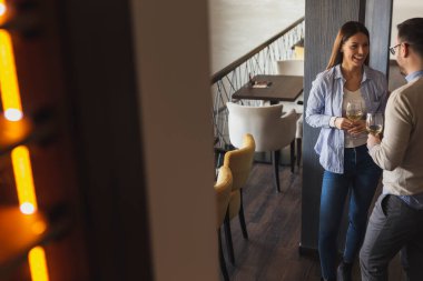 Genç çift bir restoranda buluşuyor, şarap içiyor ve öğle yemeği için bir masa beklerken hoş sohbetler ediyor.