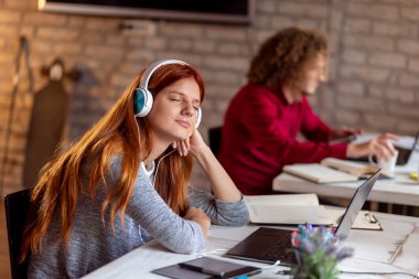 Ders çalışmaya ara vermiş güzel bir genç kız öğrenci üniversite okuma odasında dinlenirken müzik dinliyor.