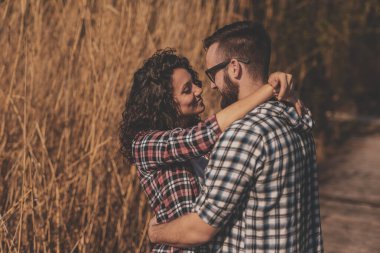 Güzel genç çift dışarıda eğleniyor, güneşli bir günü doğada geçiriyor, göl rıhtımlarında sarılıp öpüşüyor.