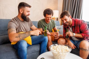 Bir grup erkek evde vakit geçirip, televizyon izleyip, patlamış mısır yiyip, bira içerek eğleniyor.