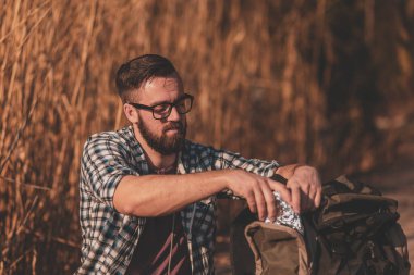 Sırt çantası ahşap göl rıhtımında oturuyor, yürüyüşe ara veriyor, doğada dinleniyor ve sandviç yiyor.