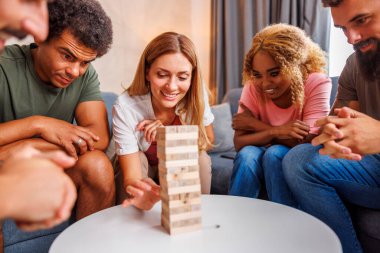 Bir grup neşeli genç arkadaş evde birlikte vakit geçiriyorlar, Jenga oynuyorlar, bir kuleden blokları sırayla kaldırıyorlar ve üstüne istifliyorlar.