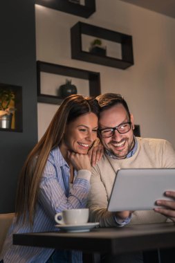 Restoran masasında oturan, kahve içen ve tablet bilgisayar kullanan güzel bir çift.