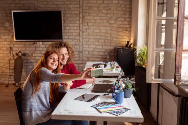 İki iş arkadaşı ofiste, akıllı bir telefonla selfie çekiyorlar; serbest çalışanlar birlikte çalışıyorlar ve tatilde eğleniyorlar.