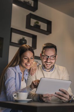 Restoran masasında oturan, kahve içen ve tablet bilgisayar kullanan güzel bir çift.