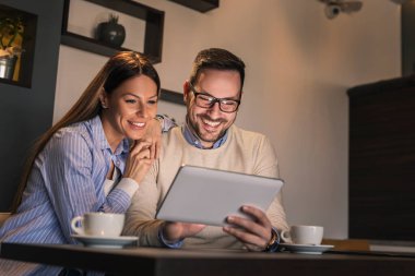 Restoran masasında oturan, kahve içen ve tablet bilgisayarda video görüşmesi yapan genç ve güzel bir çift.