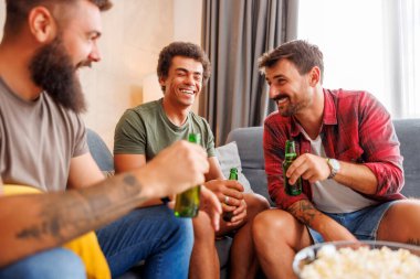Bir grup erkek evde vakit geçirip, televizyon izleyip, patlamış mısır yiyip, bira içerek eğleniyor.