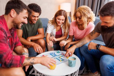 Bir grup neşeli genç arkadaş evde birlikte vakit geçirirken Ludo masası oyunu oynuyorlar.