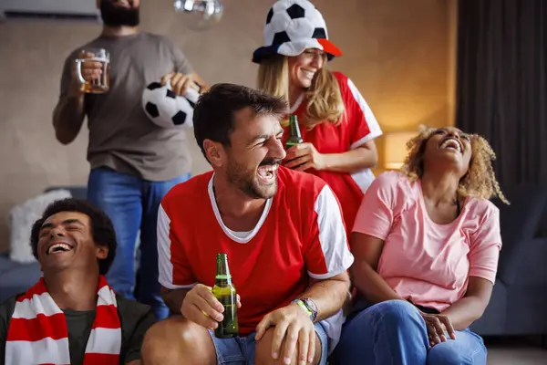 Group of cheerful football fans having fun drinking beer and watching world championship game on TV at home