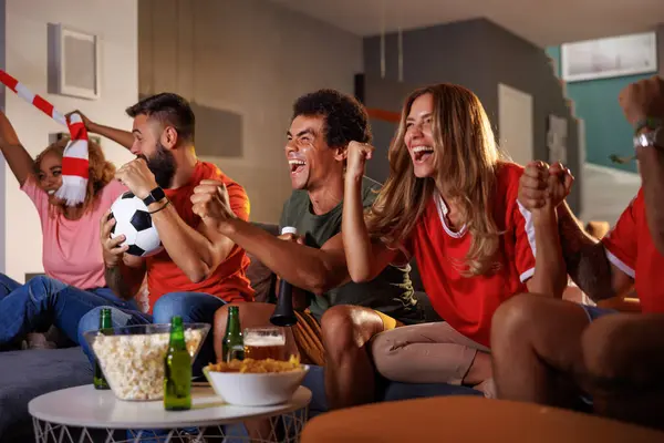 Group of football fans cheering while watching game on TV, celebrating their team scoring a goal and winning