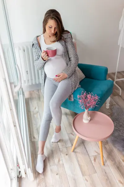 窓の近くのアームチェアに座っている美しい妊婦の肖像画 お茶を飲み 自宅でリラックス — ストック写真