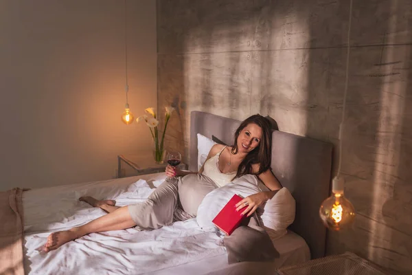 漂亮的孕妇穿着睡衣 躺在床上 早上在家里休息 喝黑莓酒 — 图库照片