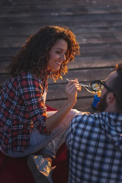 Rıhtımda kamp yapan, yemek yiyen ve günbatımının keyfini çıkaran bir çiftin yüksek açılı görüntüsü.
