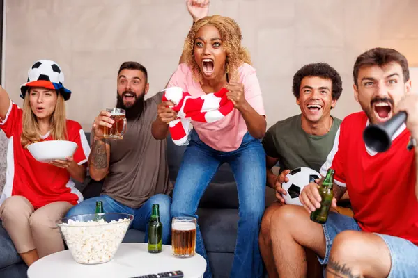 Bir grup neşeli futbol taraftarı, takımlarının evinde maç izlerken gol atmasının ardından tezahürat yapıp kutlama yapıyorlar.