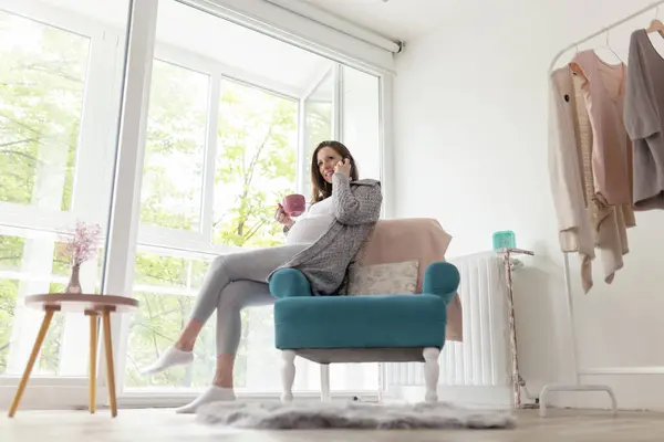 Güzel Hamile Kadın Koltukta Oturuyor Evinde Dinleniyor Çay Içiyor Telefonda — Stok fotoğraf