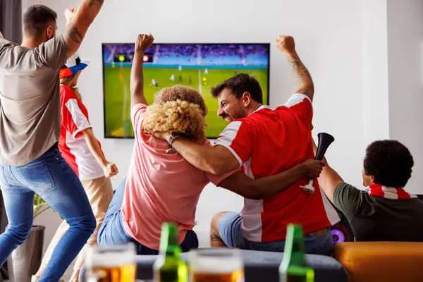 テレビでサッカーの試合を見て楽しんでいる若い友人のグループ ビールを飲むと応援 彼らのチームがゴールを獲得した後 自宅で試合を見ているサッカーファン — ストック写真