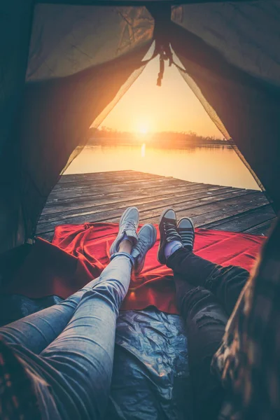 Genç çift göl rıhtımında kamp yapıyor çadırda uzanıyor gölün üzerinde güzel günbatımının tadını çıkarıyor.