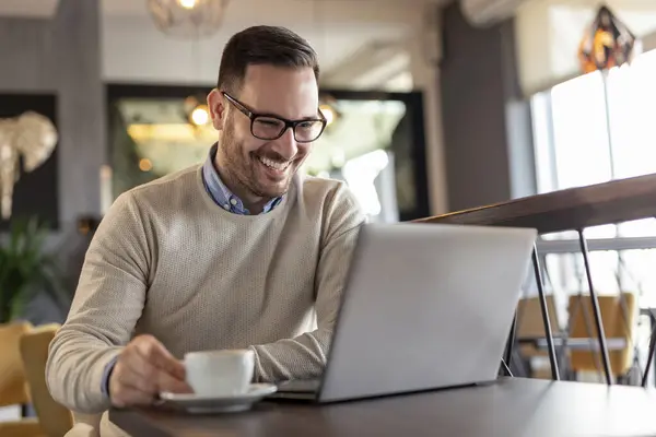 Restoran masasında oturan, kahve içen ve dizüstü bilgisayar üzerinde çalışan serbest çalışan bir erkek portresi.