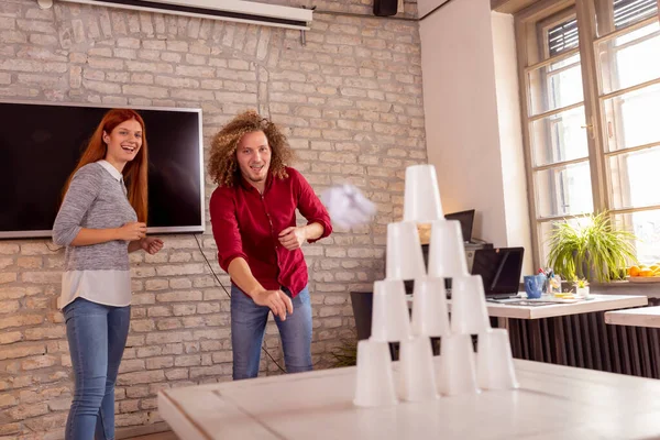 Business people having fun at the office, playing office games while on a break, tearing down a pyramid of plastic cups with a paper ball