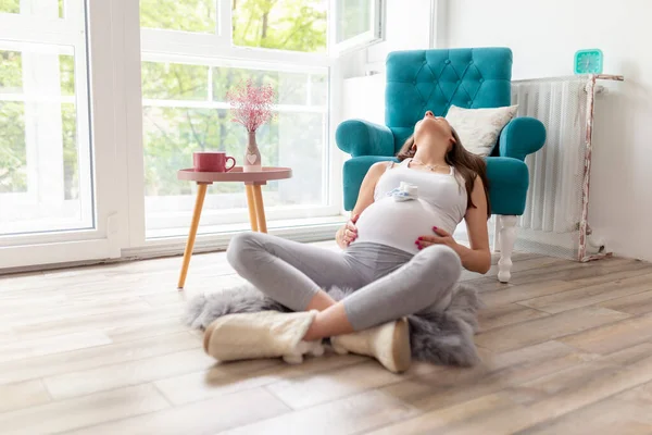 自宅でリラックスし 赤ちゃんを期待して 美しい妊娠中の女性 アームチェアの隣に座っている妊婦 彼女の腹に小さな赤ちゃんの靴を抱き — ストック写真