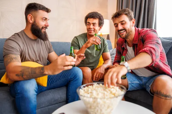 Bir grup erkek evde vakit geçirip, televizyon izleyip, patlamış mısır yiyip, bira içerek eğleniyor.
