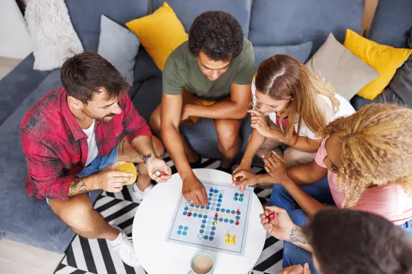 Bir grup neşeli genç arkadaşın evde birlikte vakit geçirirken Ludo masası oyunu oynamalarının yüksek açılı görüntüsü.