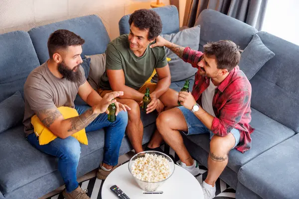 Bir grup erkek arkadaşın evde birlikte vakit geçirip, televizyon izleyerek, patlamış mısır yiyerek ve bira içerek eğlendiği geniş açılı bir manzara.