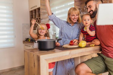 Güzel, mutlu bir aile birlikte yemek pişiriyor, mutfak tezgahında oturuyor ve evde boş vakitlerin tadını çıkarıyor.