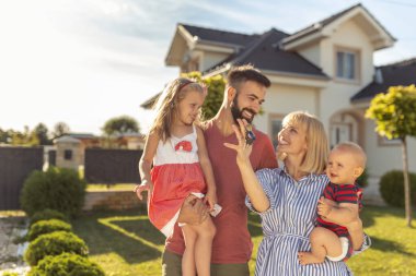 Güzel, mutlu bir aile yeni evlerinin önünde duruyor, parnetler çocukları ve anahtarları tutuyor.