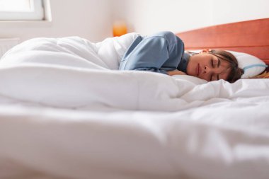Sabahları beyaz çarşaflarla kaplı pijama giyen güzel bir kadının alçak açılı görüntüsü.