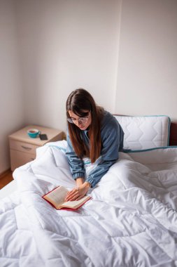 Sabahları pijama giyen, kitap okuyan ve evde dinlenen güzel ve düşünceli genç bir kadın.