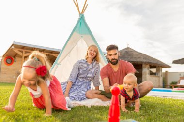 Mutlu bir aile, güneşli bir yaz gününü arka bahçede kamp yaparak, ebeveynler çocuklarıyla bowling oynayarak, top oynayarak ve lobutları devirerek geçirir.