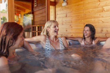 Bir grup neşeli genç kadın otel spa merkezindeki jakuzide dinleniyor, tatildeyken eğleniyorlar.