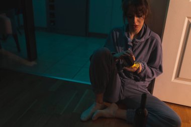 Kadın uyuşturucu bağımlısı mutfakta sarhoş bir şekilde oturuyor, şarapla birlikte bir avuç dolusu hap alıyor; madde bağımlılığı, depresyon ve intihar konsepti