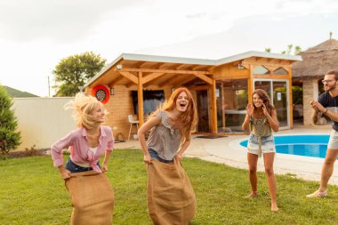 Bir grup neşeli genç arkadaş arka bahçede havuz kenarında atlama yarışına katılırken eğleniyorlar.