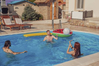 Bir grup arkadaş sıcak bir yaz gününde dışarıda eğleniyorlar, yüzme havuzunda voleybol oynuyorlar, yaz tatilinde dinleniyorlar.