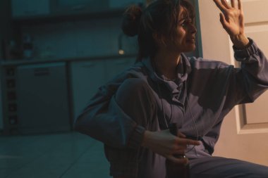 Kadın alkolik, makyajla karanlıkta yerde oturuyor, şişeden şarap içiyor ve ağlıyor.