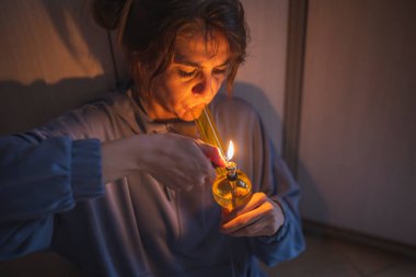 Bunalımlı genç bir kadın karanlıkta yerde oturuyor, esrar içiyor, nargileyle esrar içiyor, kadın nargileyle marihuana içiyor.