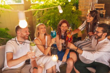 Bir grup neşeli genç arkadaş bir doğum günü partisinde eğleniyor, kadeh kaldırıyor ve kokteyl içiyor. 