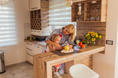 Güzel anne-kız mutfakta yemek pişiriyor, mutfak tezgahında sebze kesiyor.