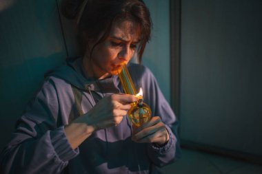 Bunalımlı genç bir kadın karanlıkta yerde oturuyor, esrar içiyor, nargileyle esrar içiyor, kadın nargileyle marihuana içiyor.